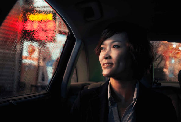 A woman in a car looks out at a rainy urban neon lit street