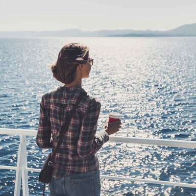 A woman stands by the rail of a ferry with coffee