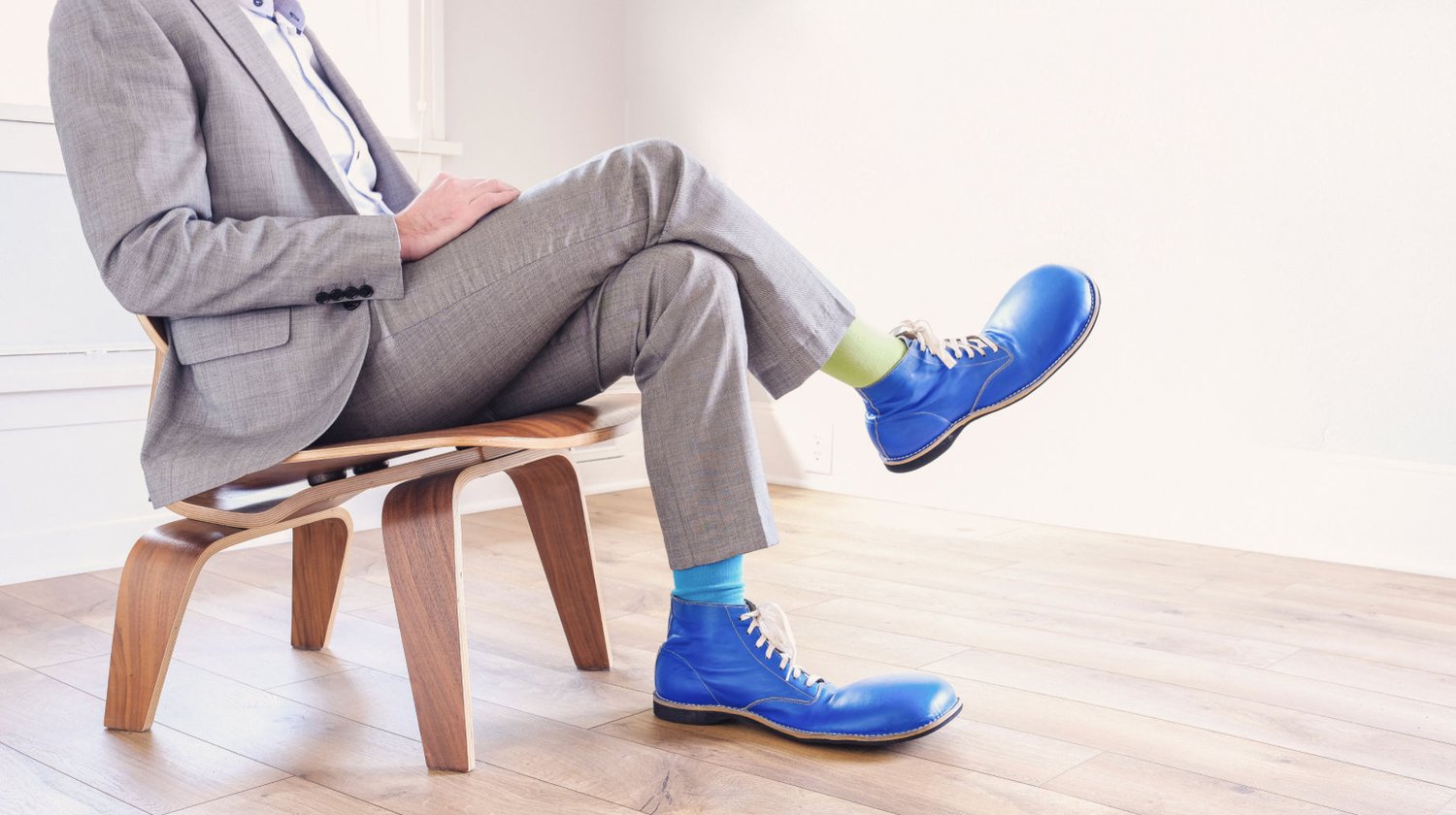 Business man sitting in grey suit and blue clown shoes