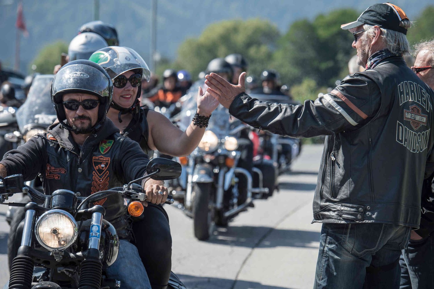 Couple on Harley-Davidson motorcycle hi-fiving spectator