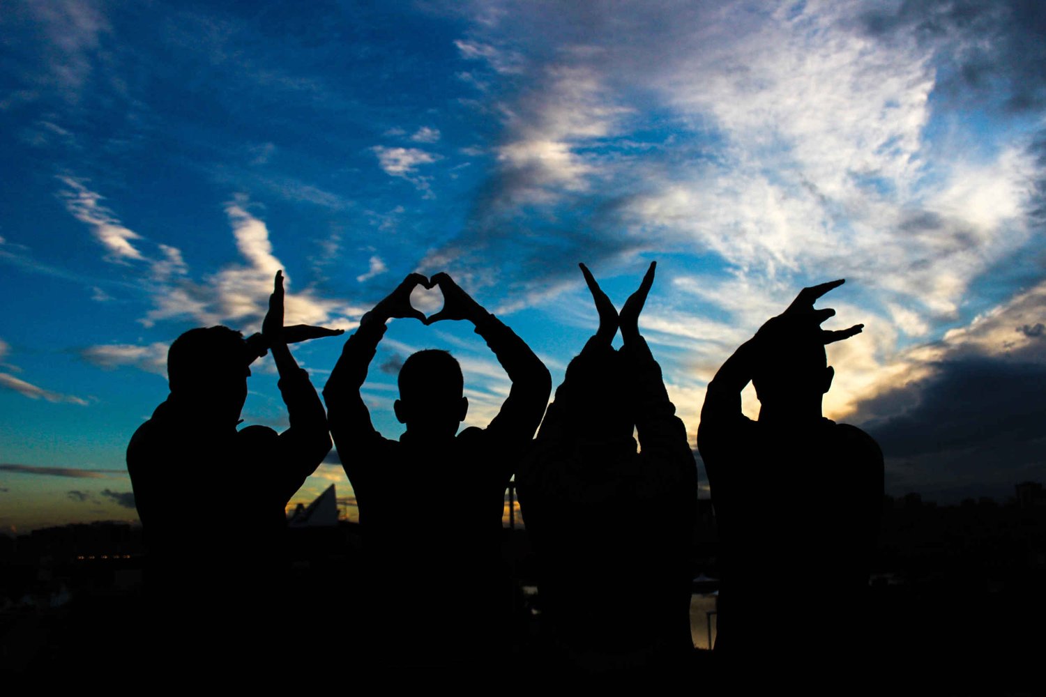 Group of people creating LOVE sign with their hands at sunset
