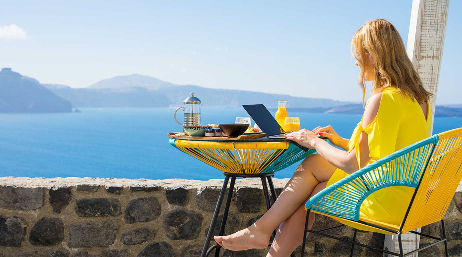 Woman at laptop with breakfast overlooking the sea