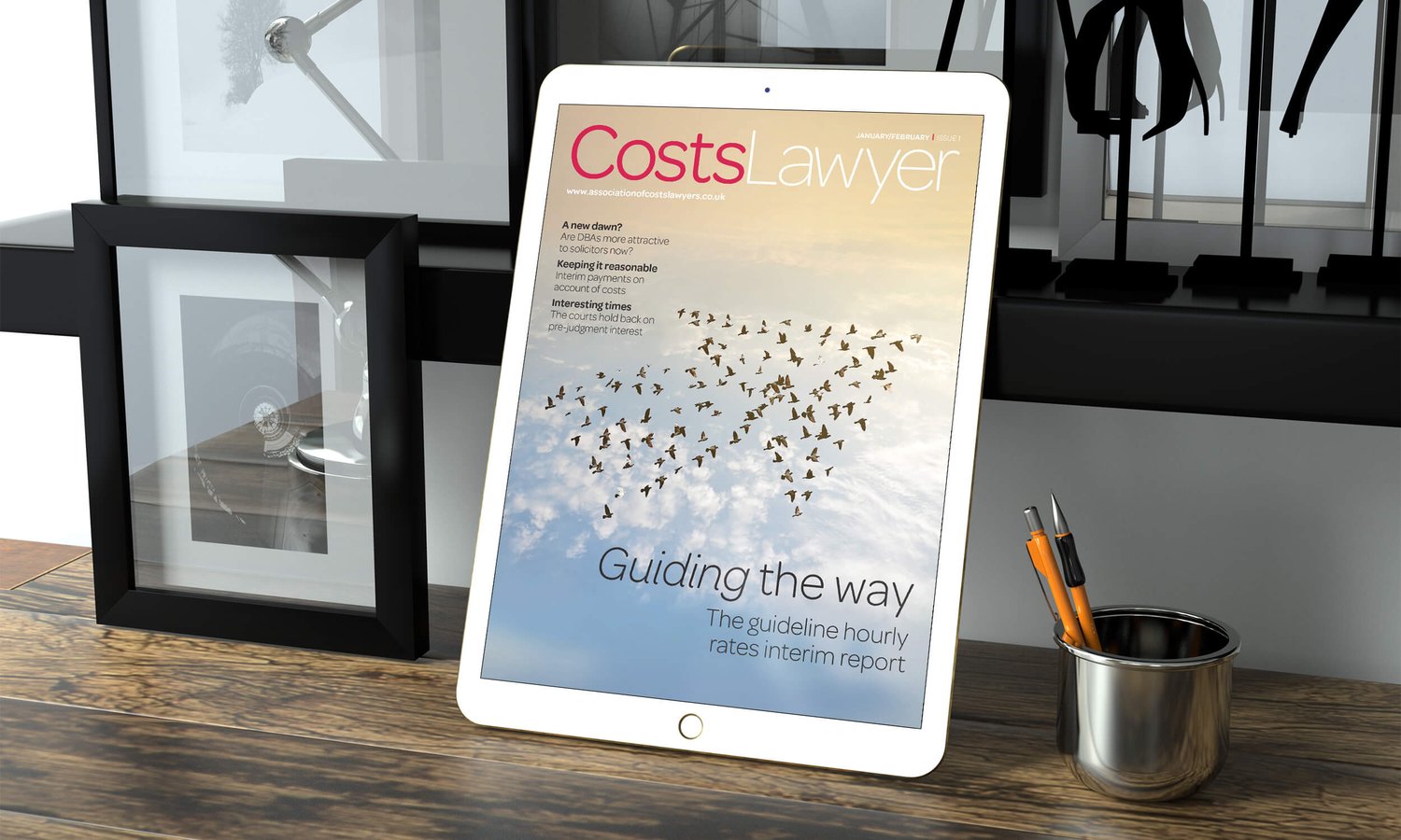 A tablet leaning upright on a desk displaying the cover of Costs Lawyer magazine
