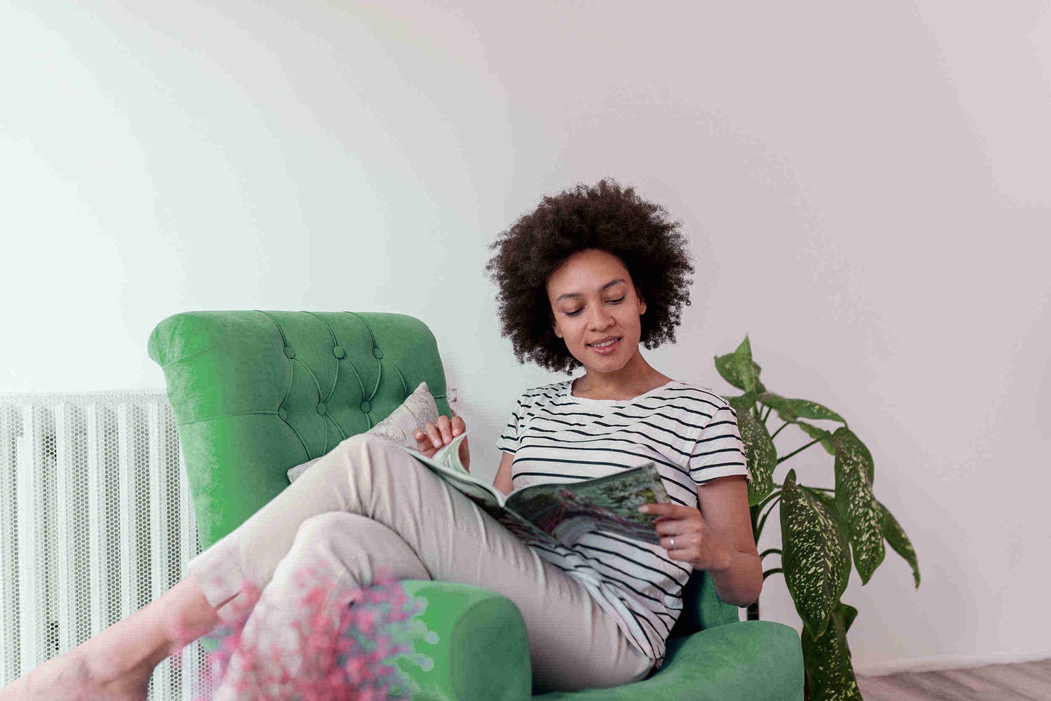 Woman sitting with her legs over the arm of a chair reading a magazine.