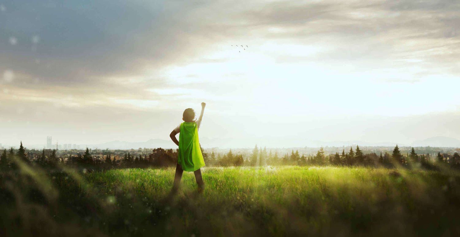 Little boy wearing green cape punching the air in the field