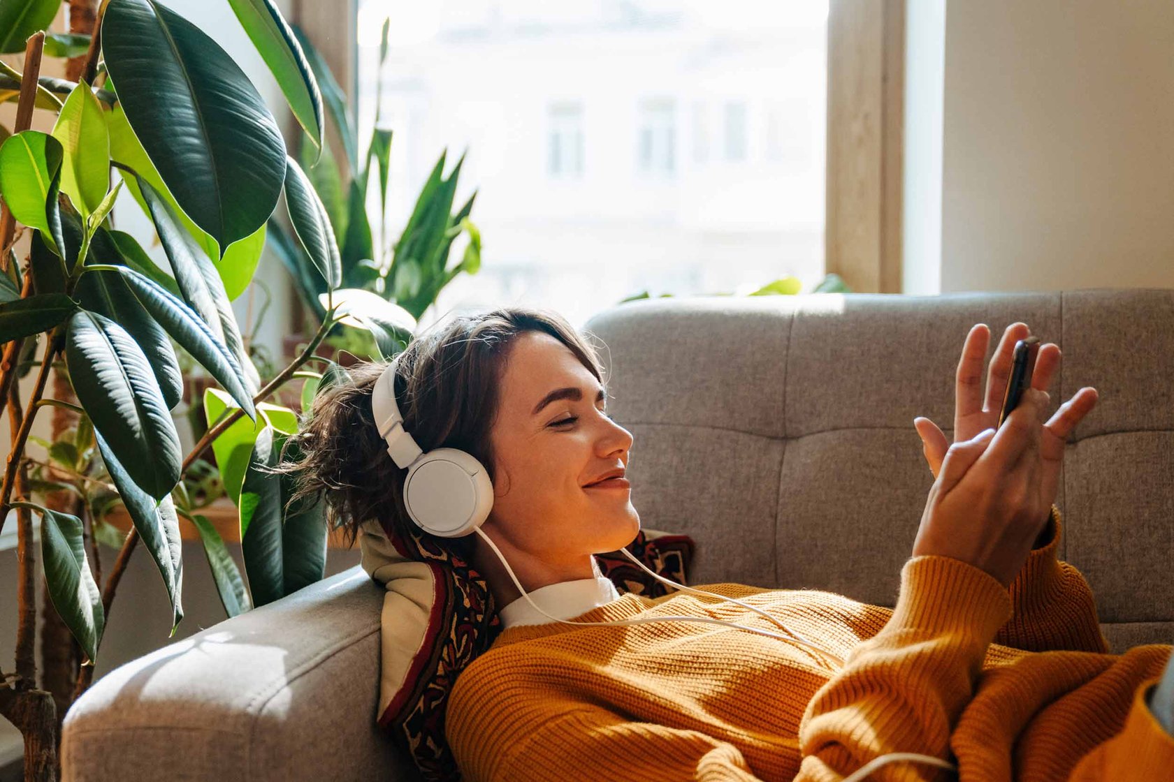 A lady laying on a sofa with headphones on.