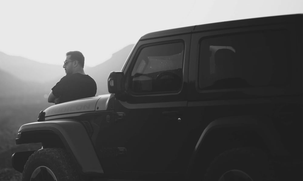 A man leans on his jeep and surveys a landscape