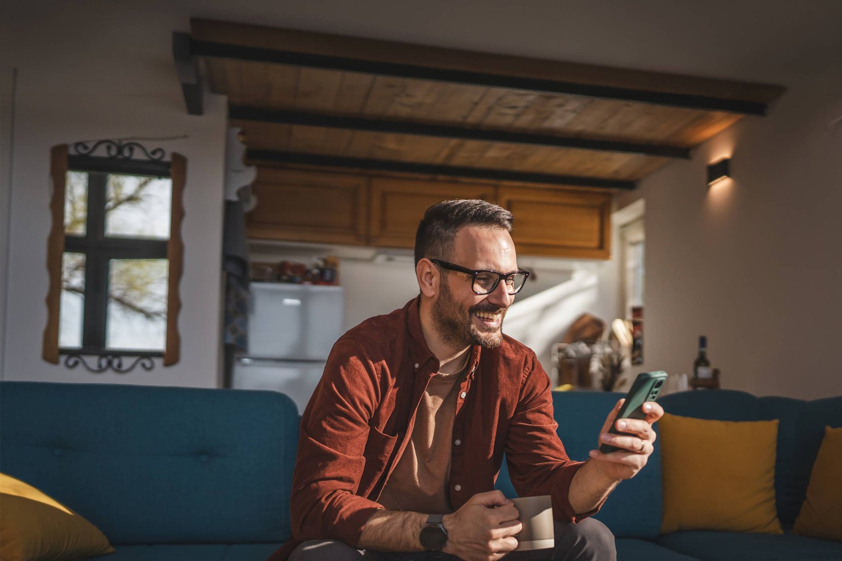 A man sat on a sofa smiling looking at his mobile phone.