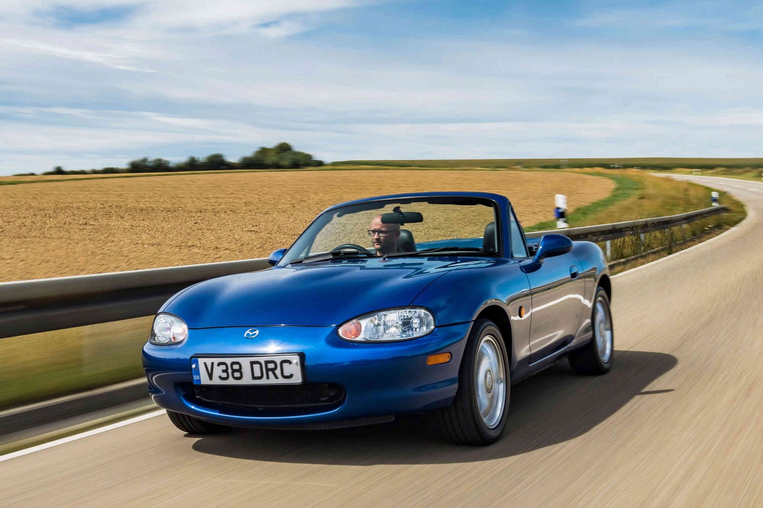 Image of blue open top MX-5 driving along country road 