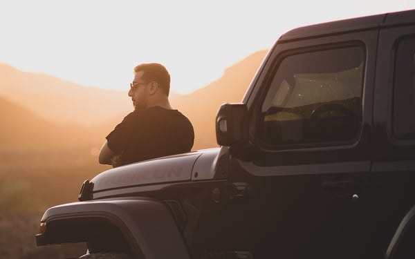 Man leaning on Jeep hood looking at sunset