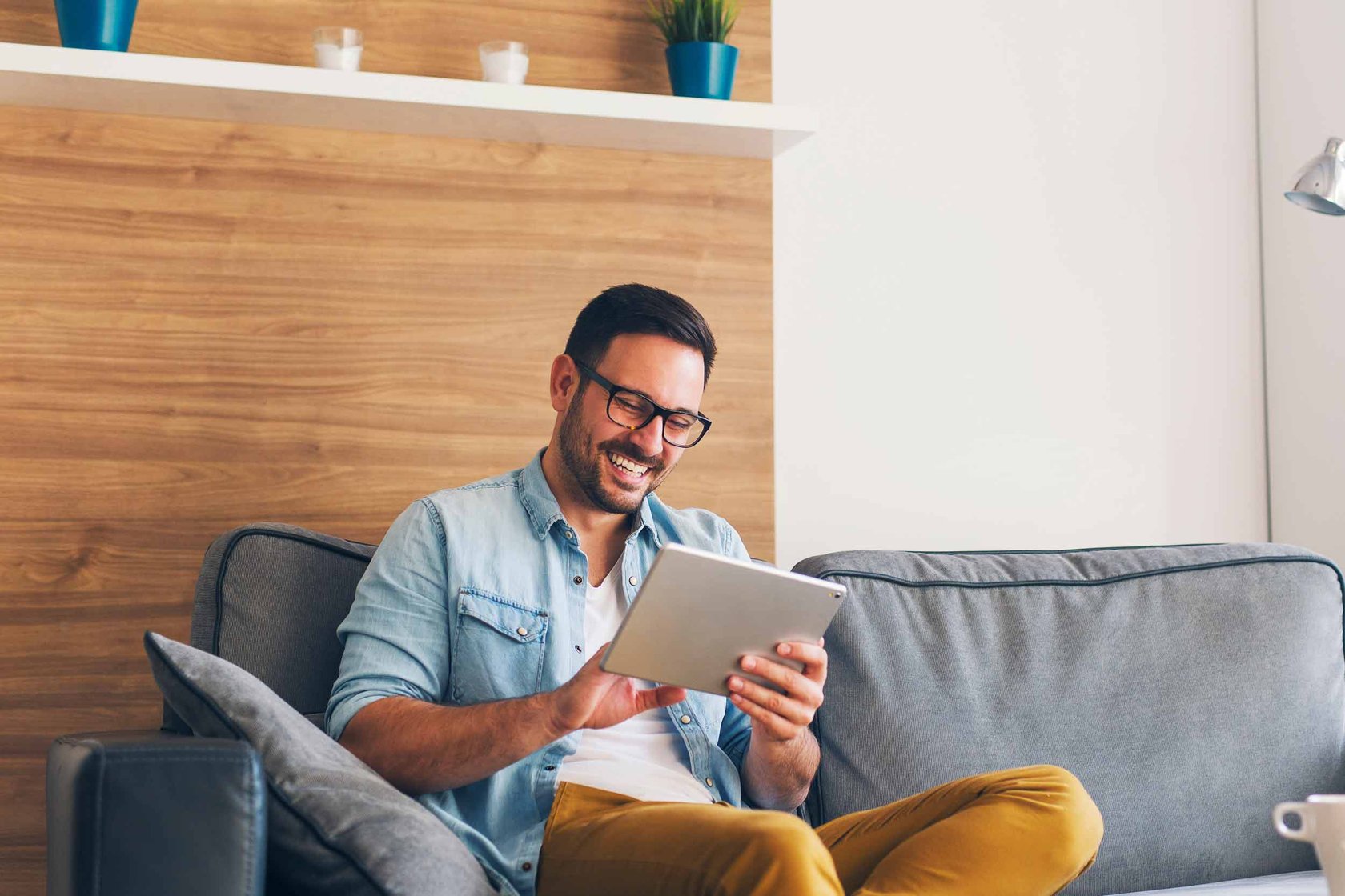 A man sat down laughing reading a tablet.